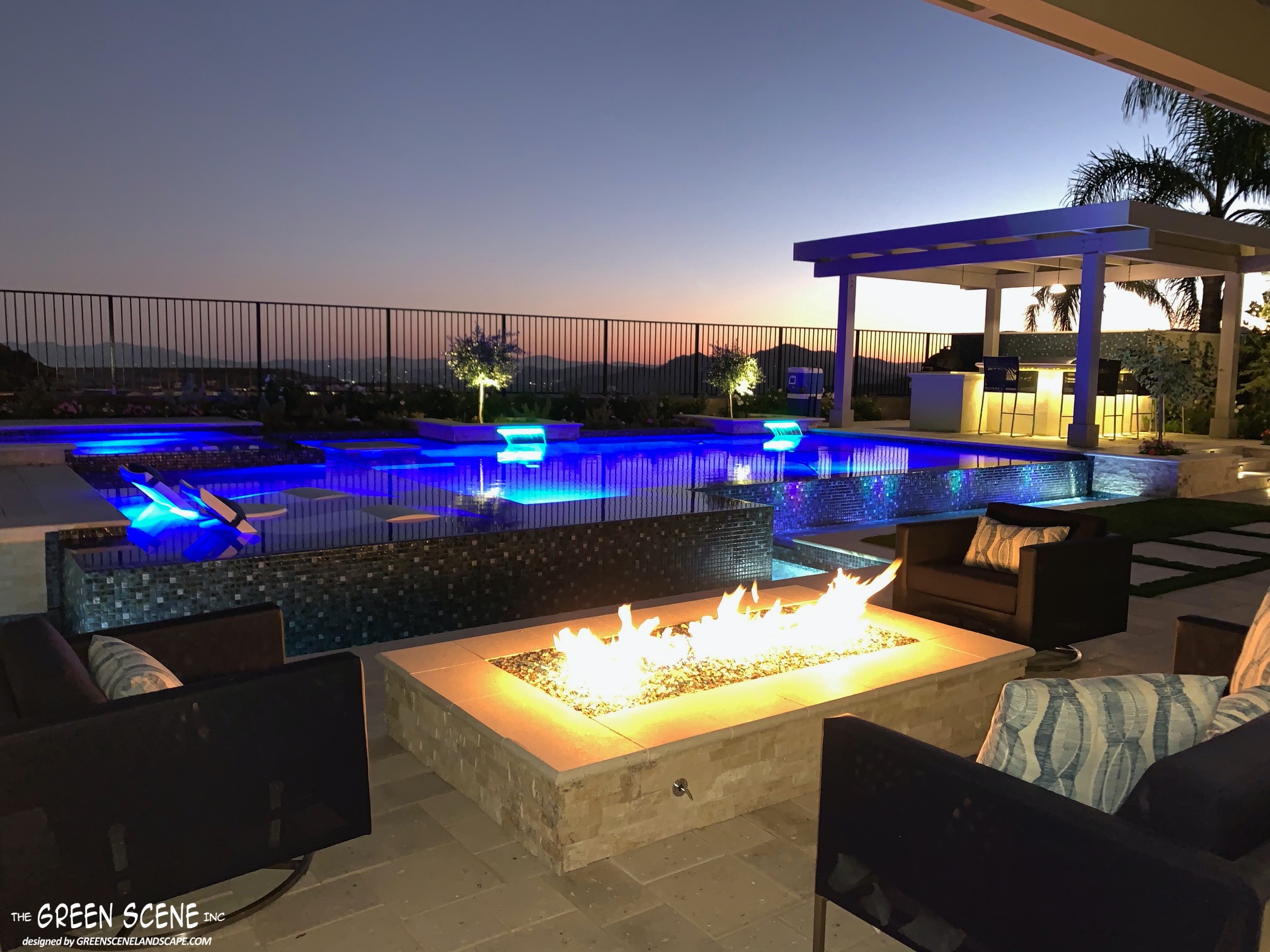 backyard with nightscaping in pool, outdoor kitchen, and fire pit